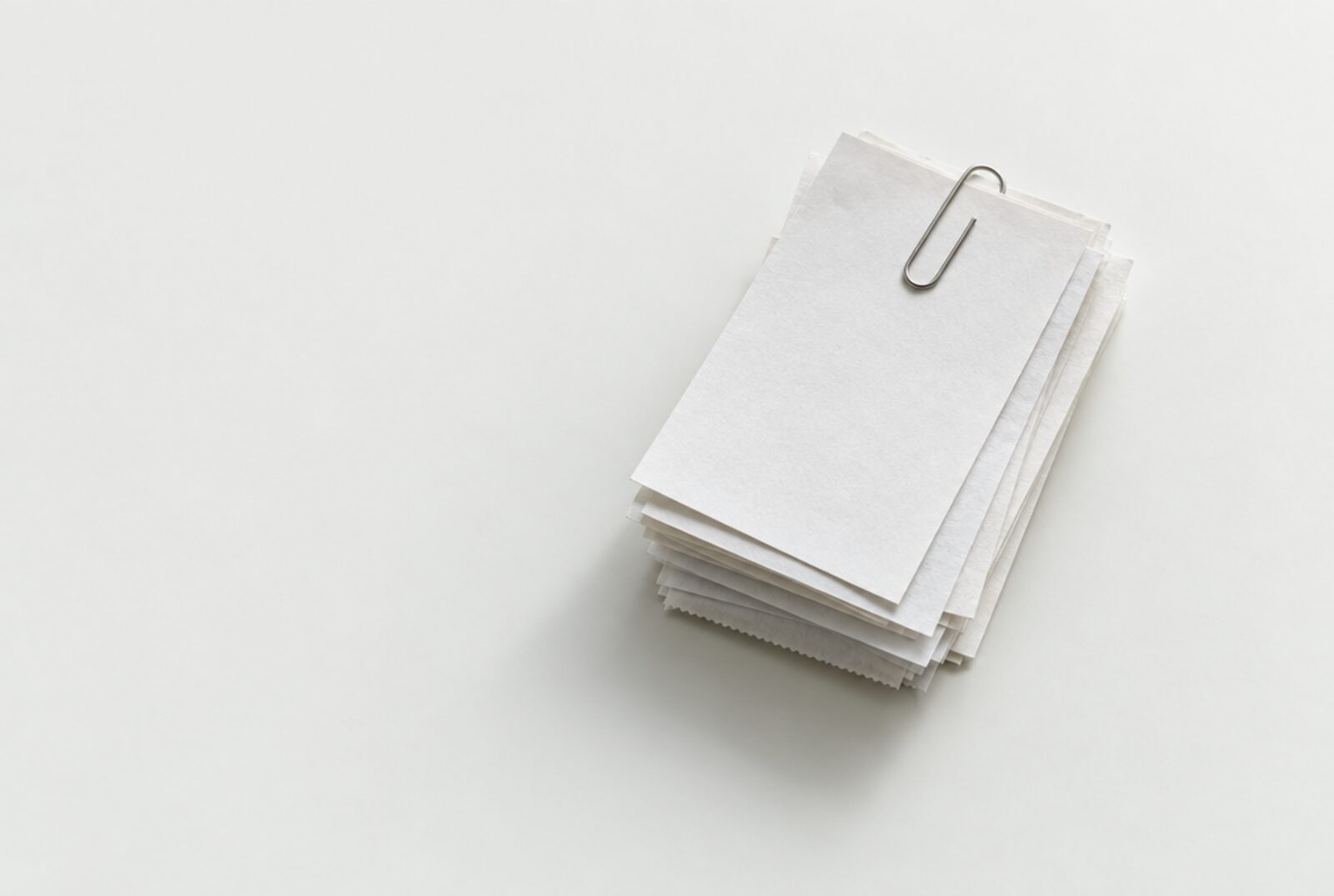 A small stack of blank paper slips held by a steel clip on a pale porcelain surface.